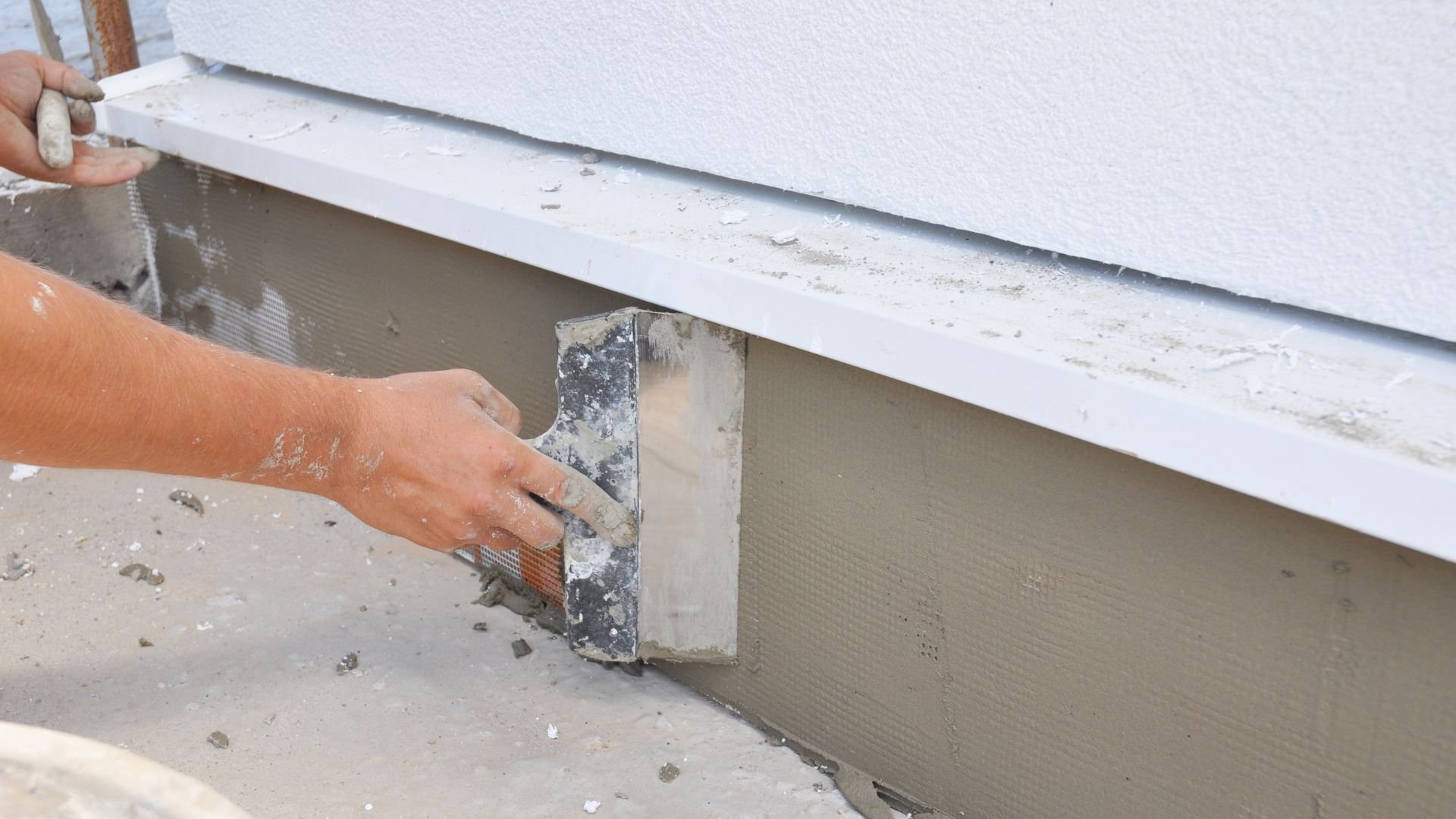 Worker applying cement render to wall using plastering trowel