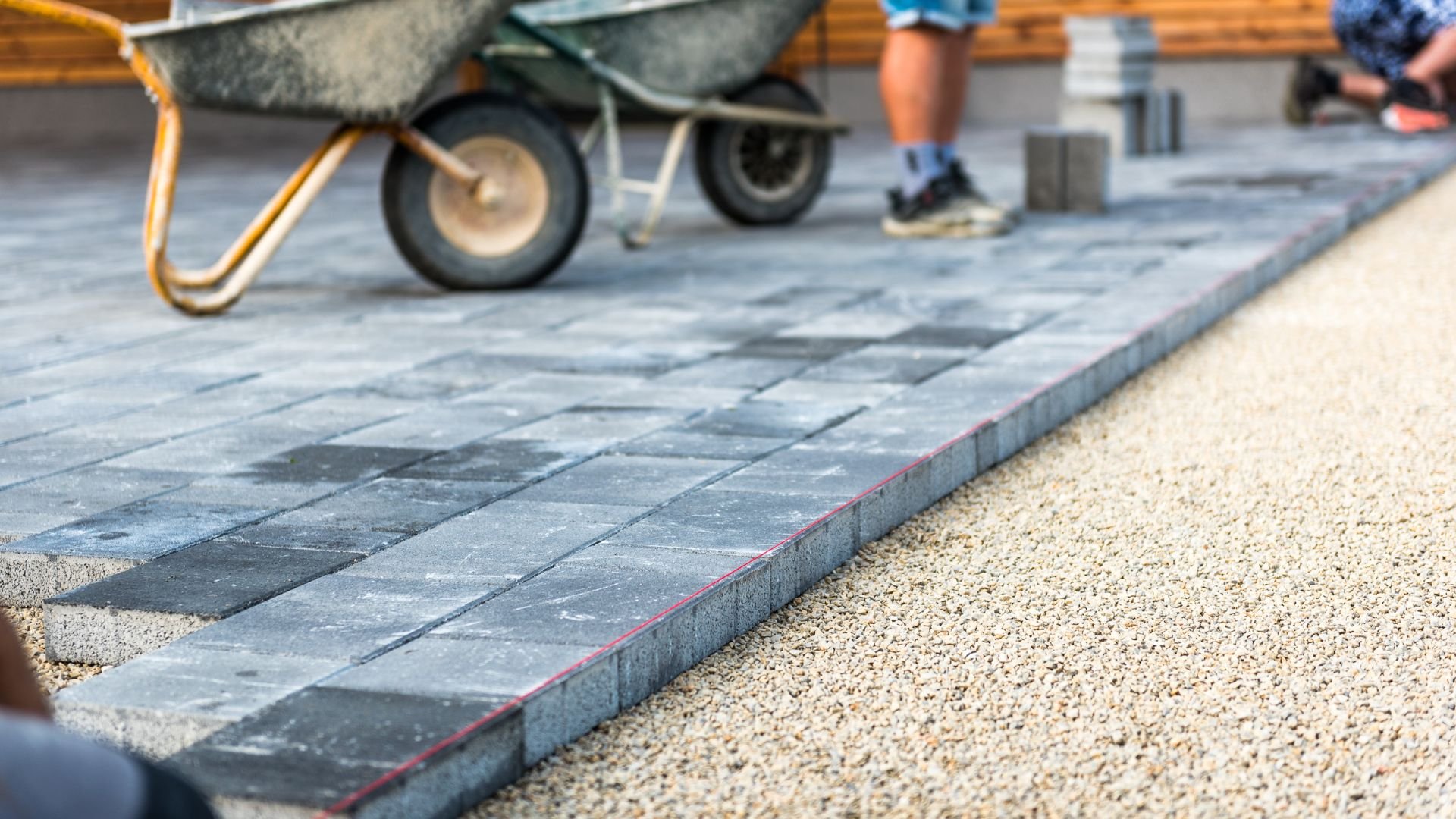 Paver stones being laid with wheelbarrow and worker's feet visible