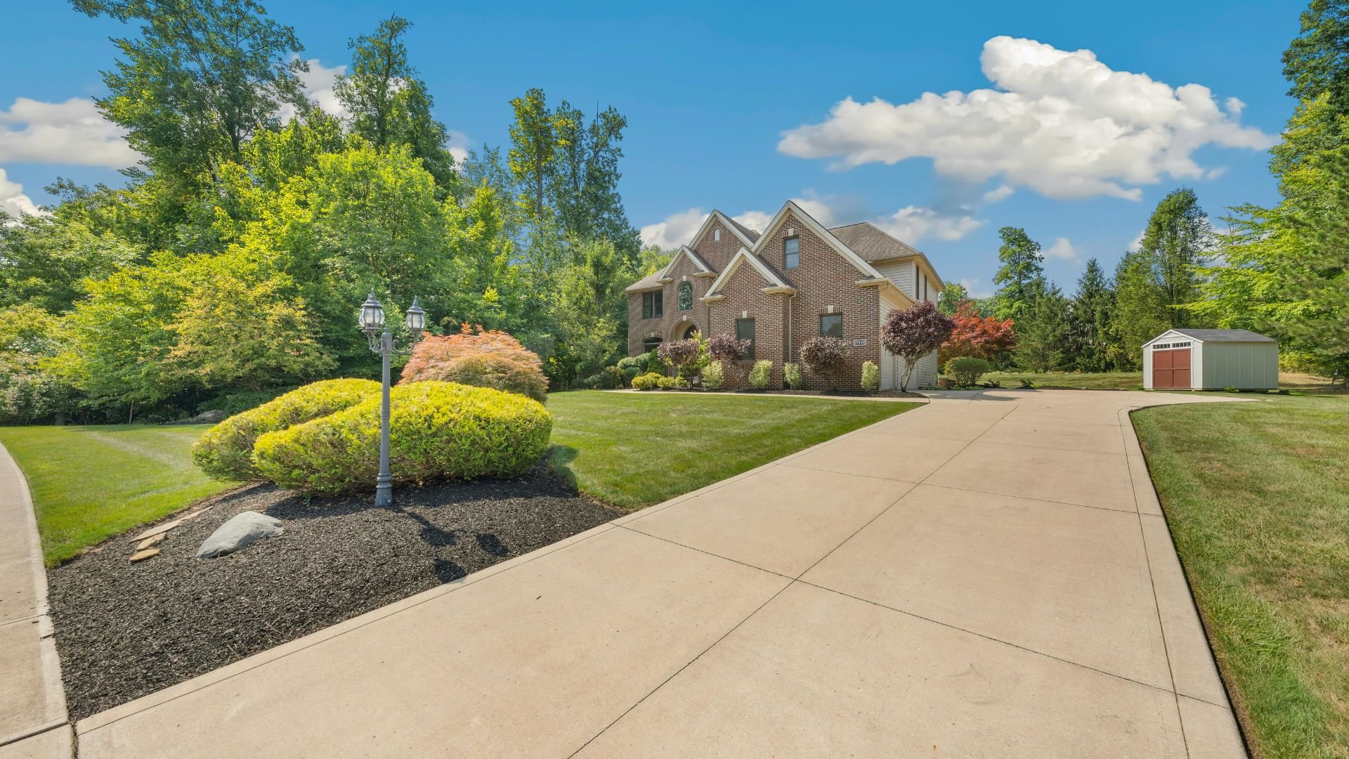 Brick house with manicured lawn, landscaped garden, and shed on sunny day