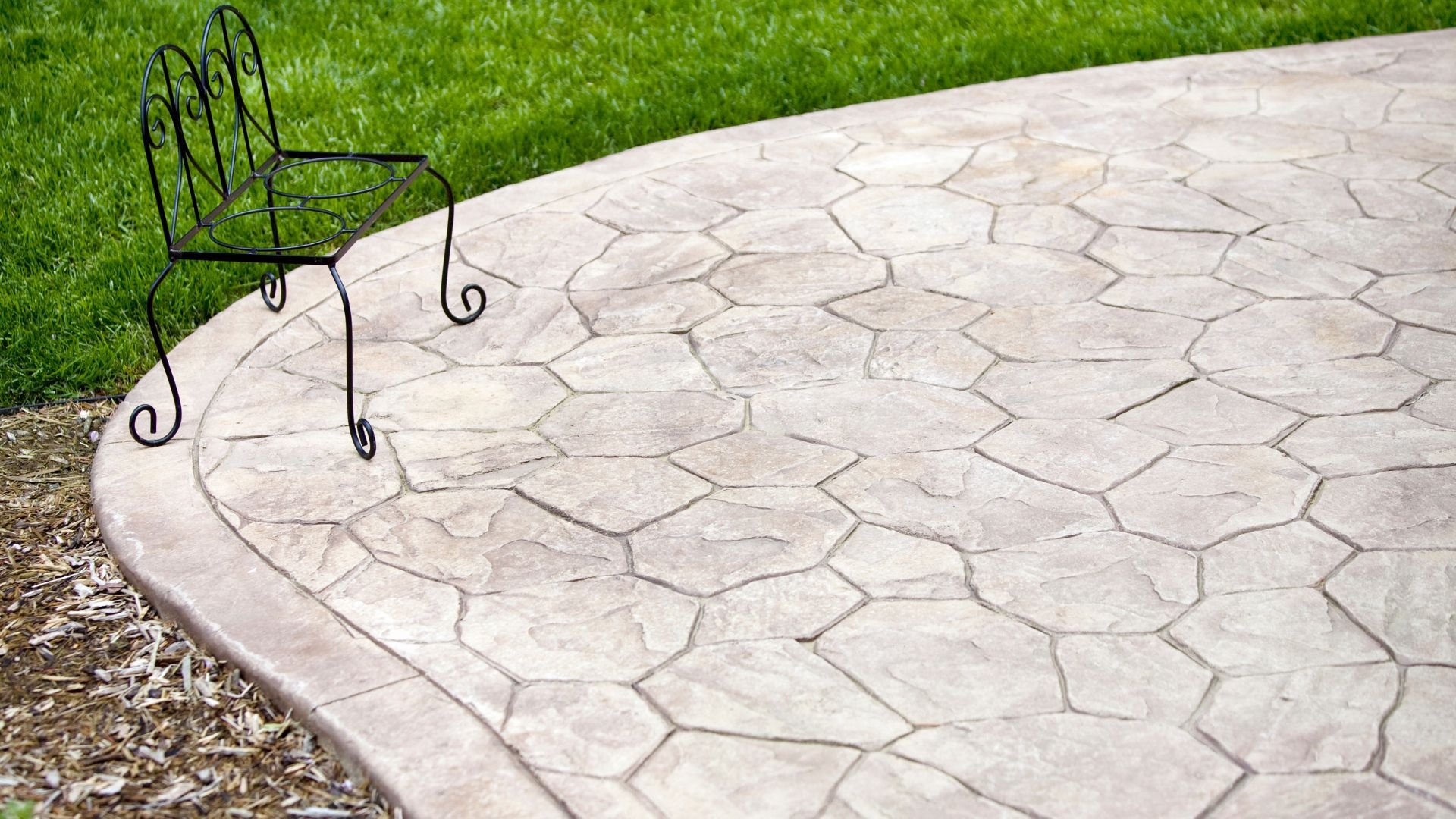 Wrought iron chair on textured stone patio with green grass border