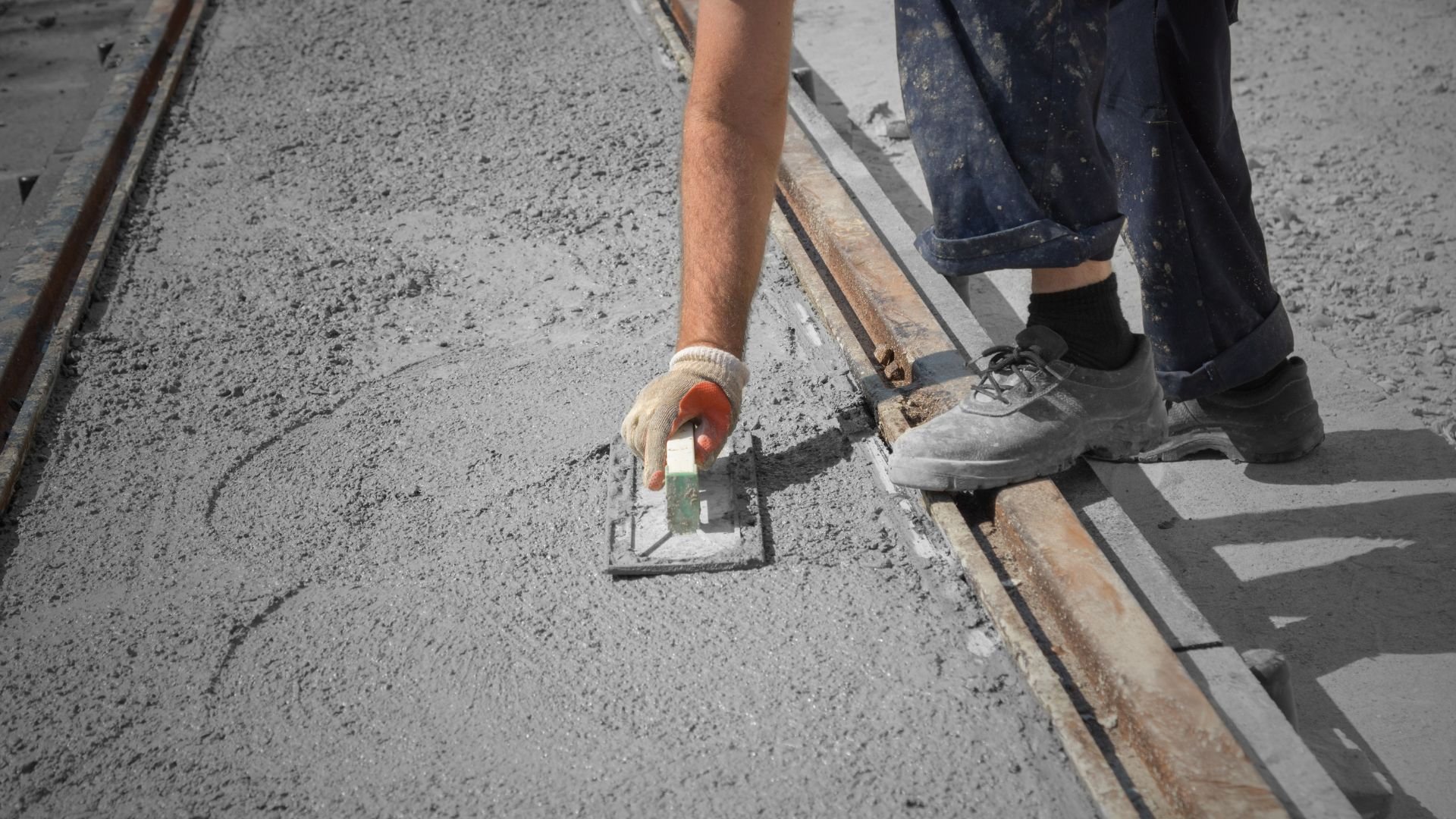 Worker smoothing wet concrete with trowel on construction site